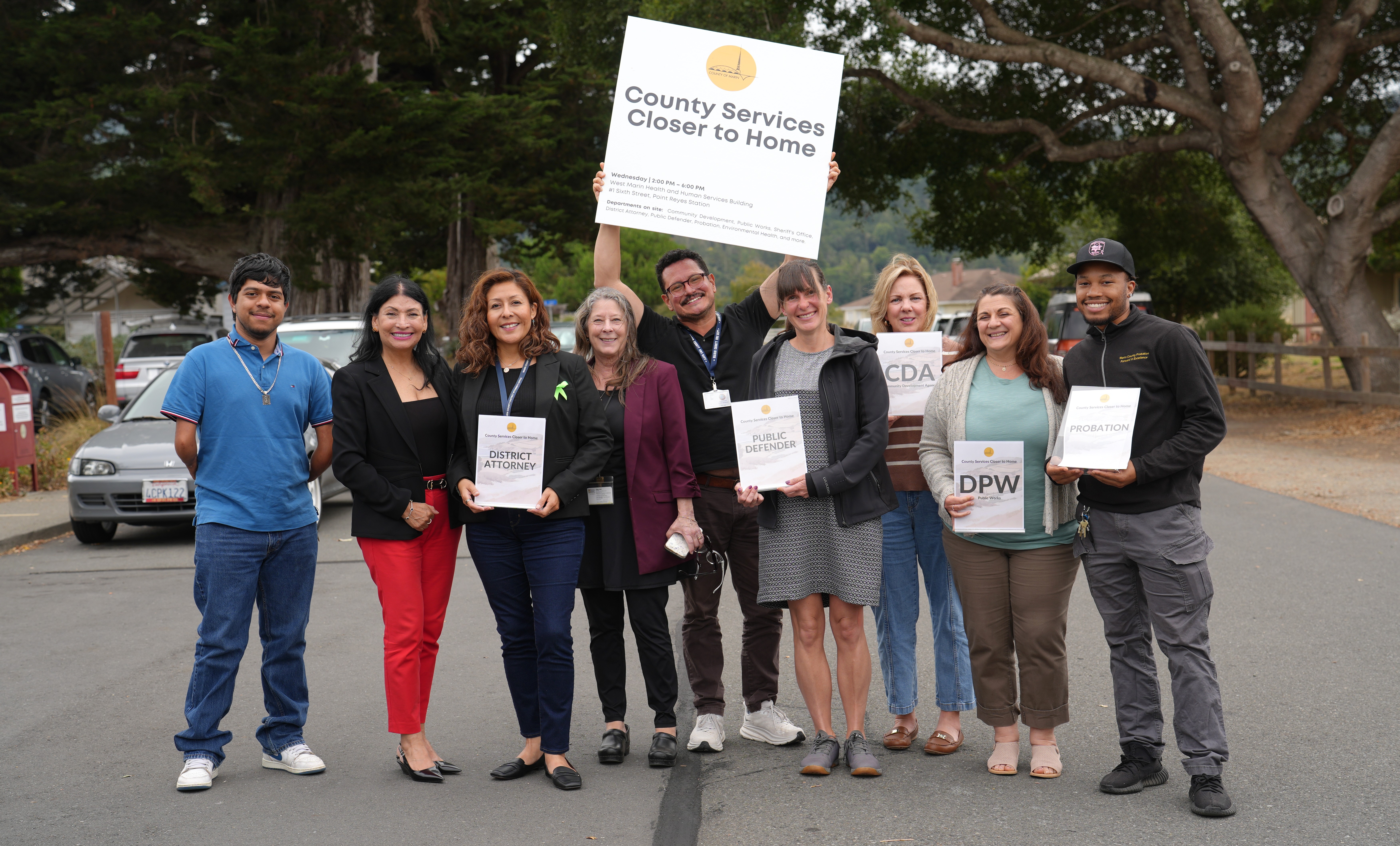 Ten people pose and smile as one person holds up the County Services Closer to home sign.