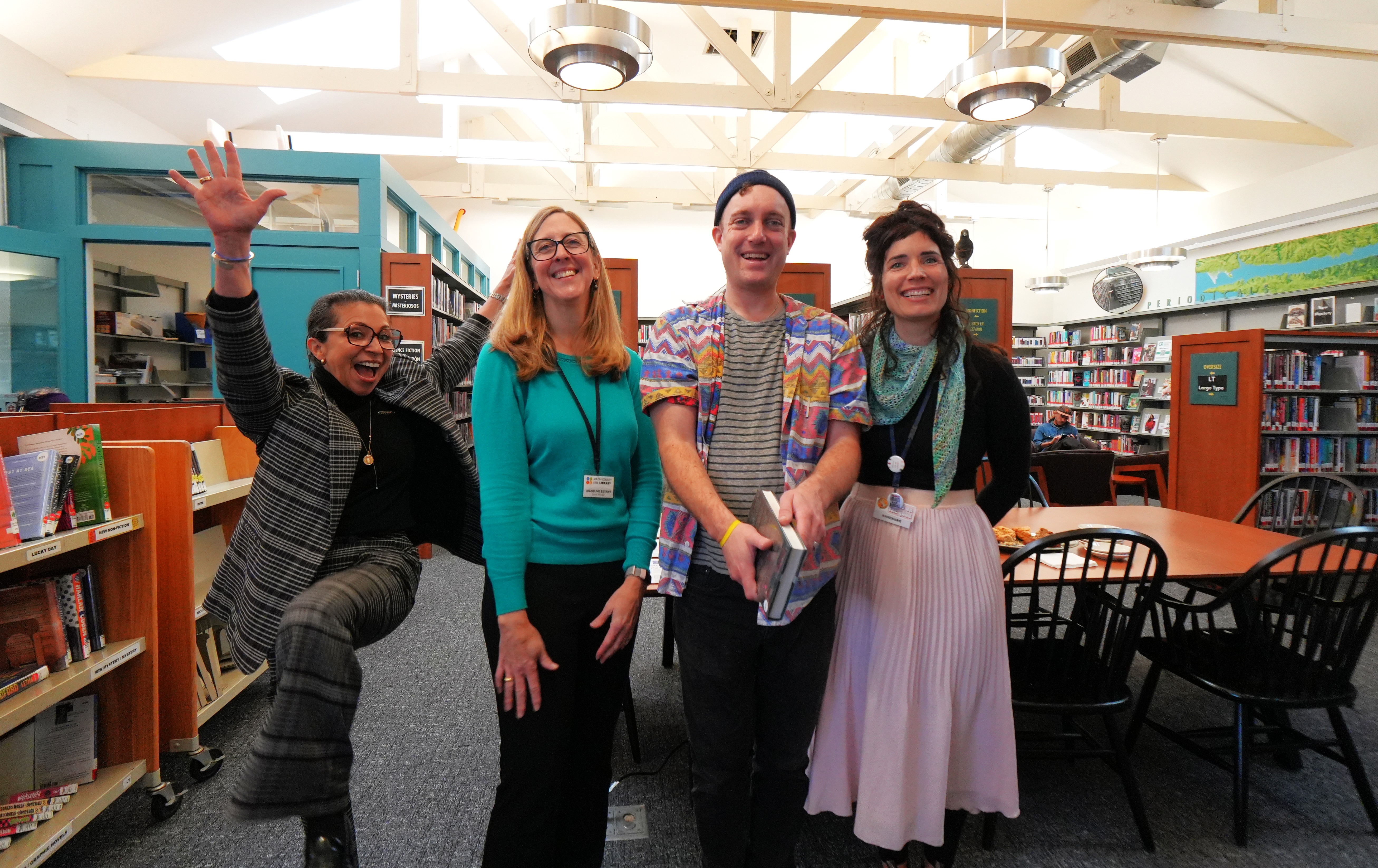 Four employees smile and gesture inside one of the renovated library branches.