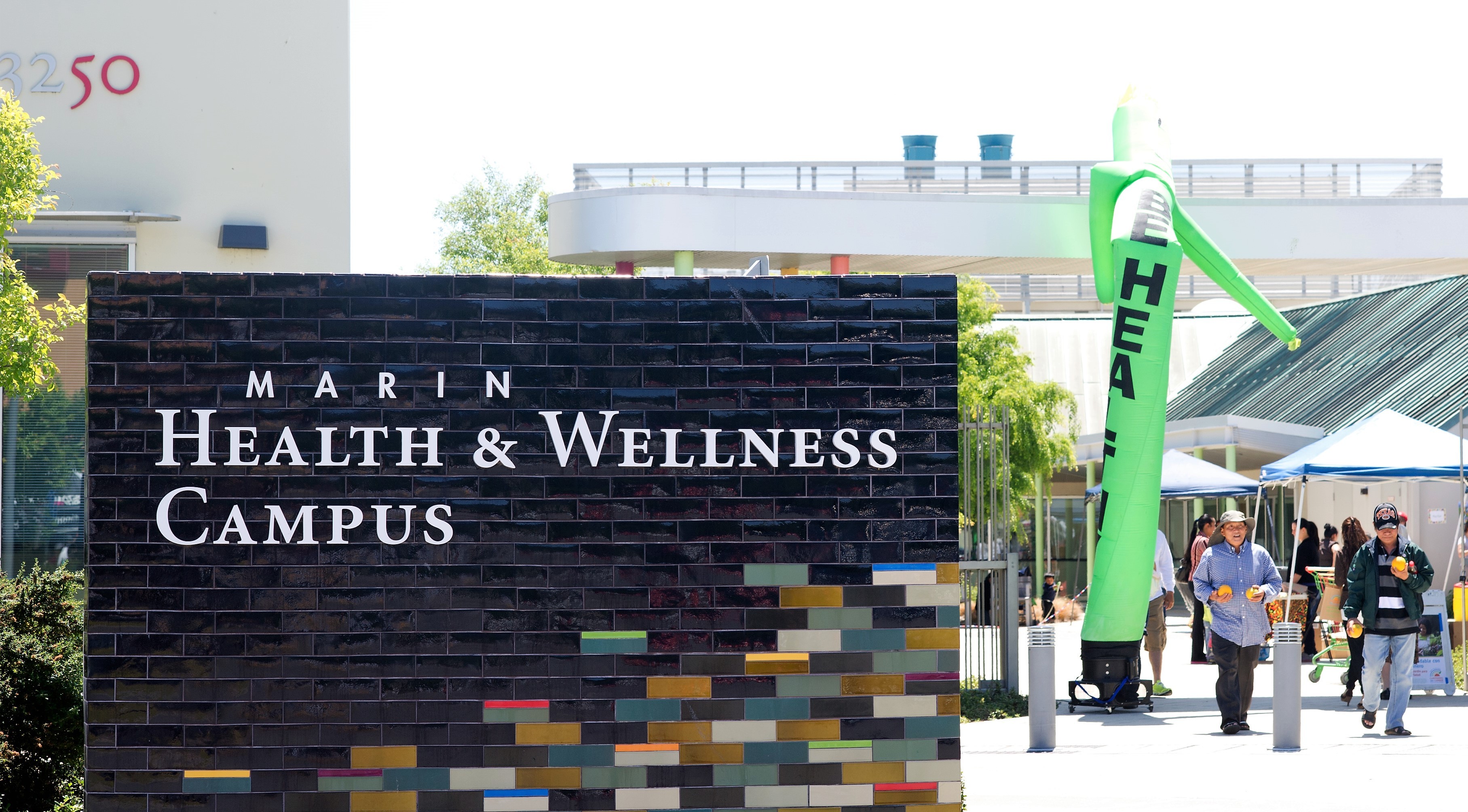 Two men walk next to the big sign outside the Marin County Wellness Campus, run by Marin County Public Health.