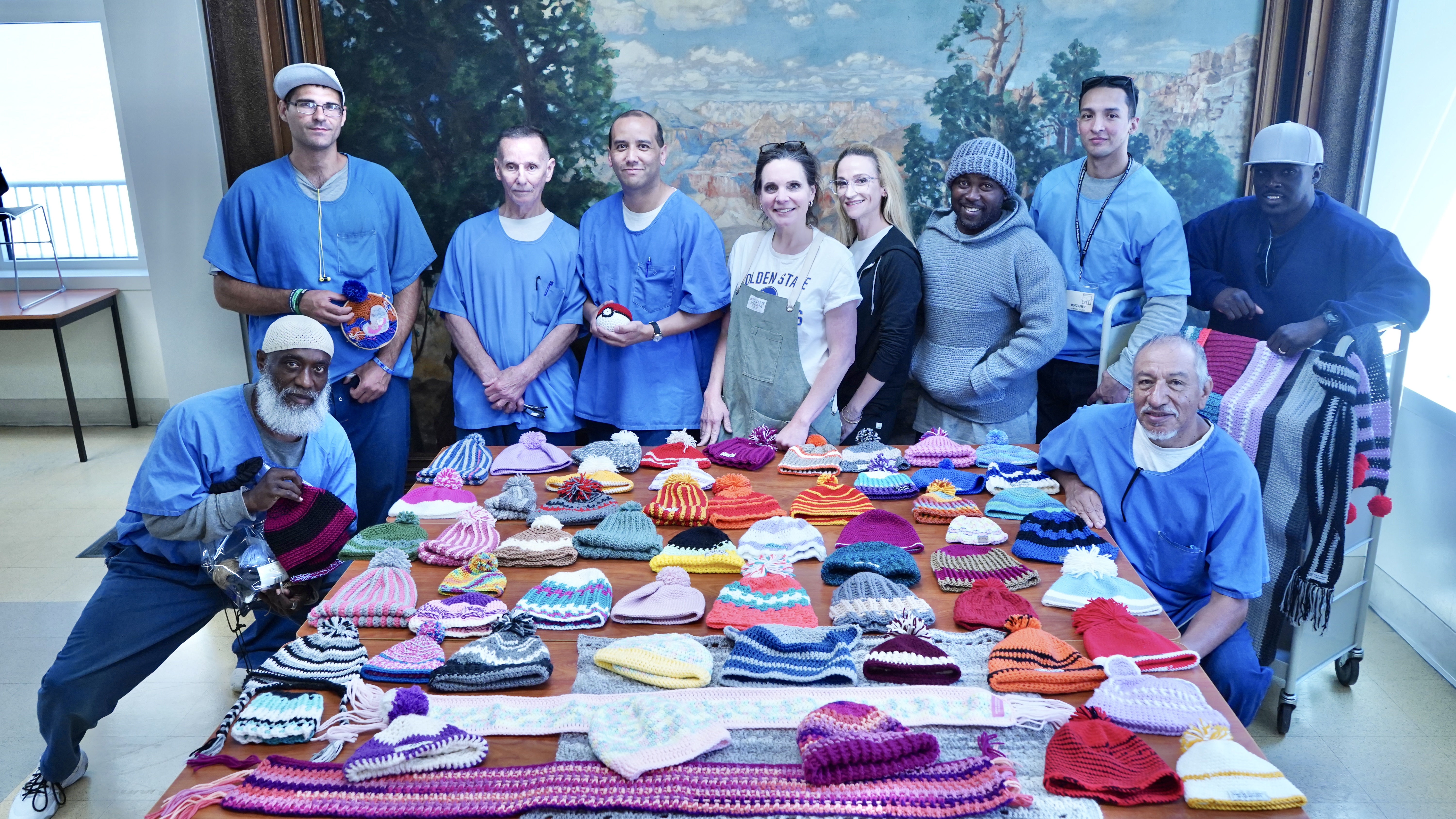About 20 people pose around a table that displays their works of art.