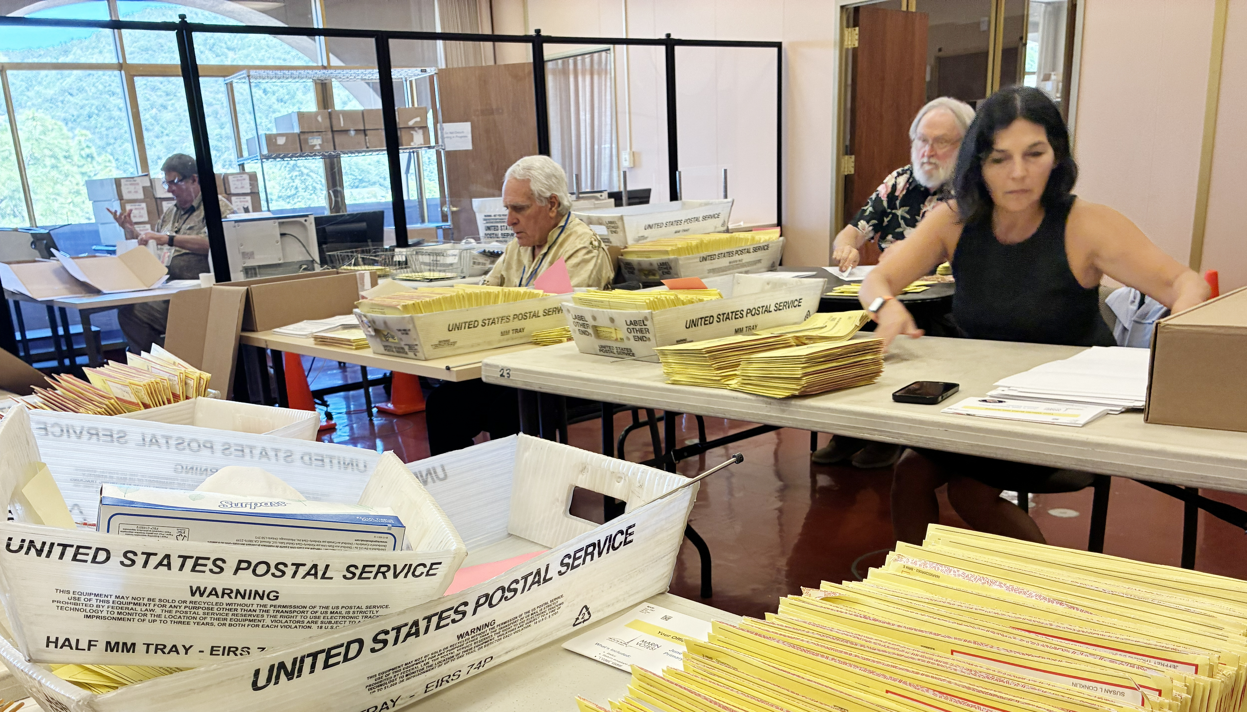 several election workers sort through ballots on a table.