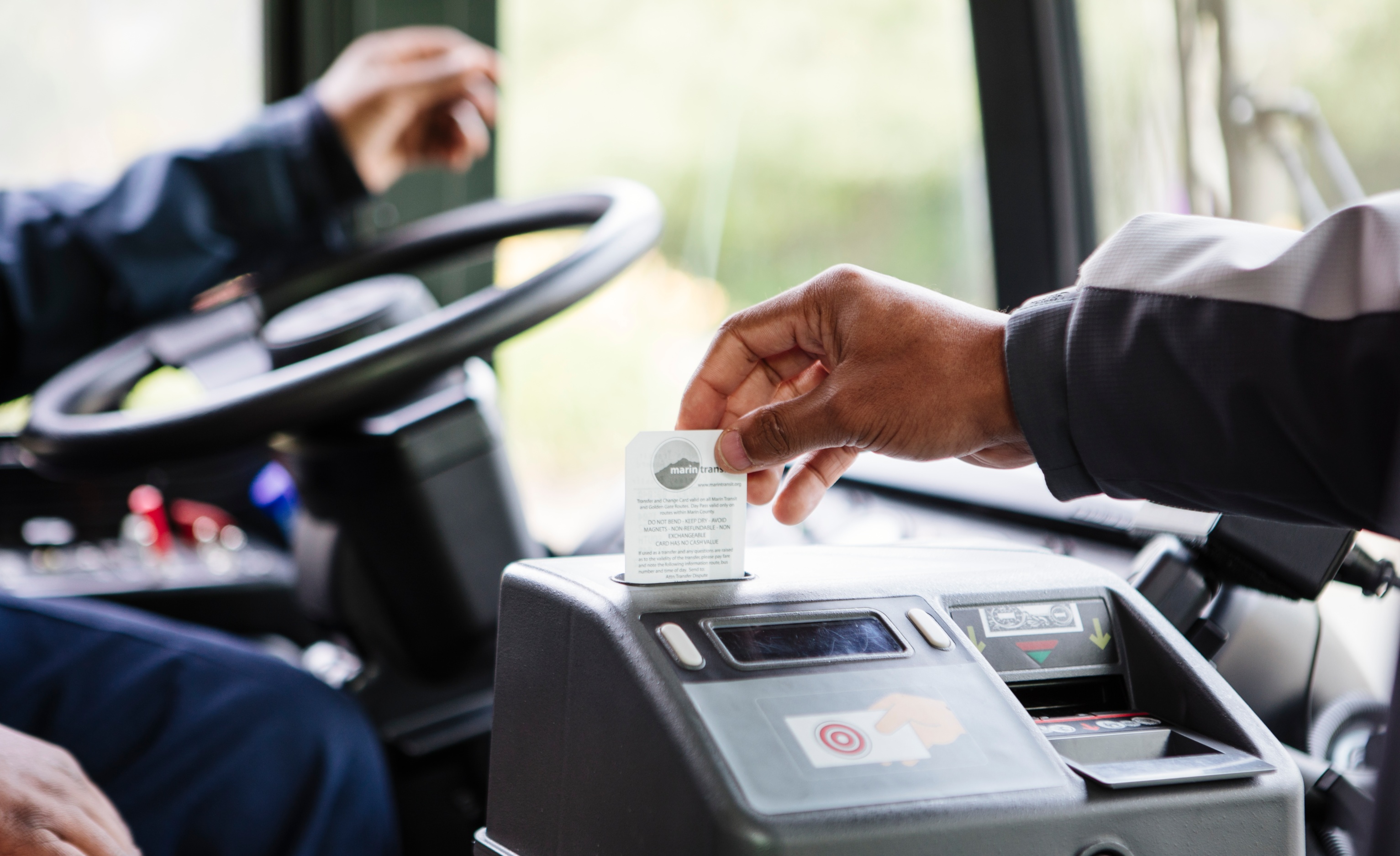 A person's hand is shown swiping a card in a scanner on a transit bus.