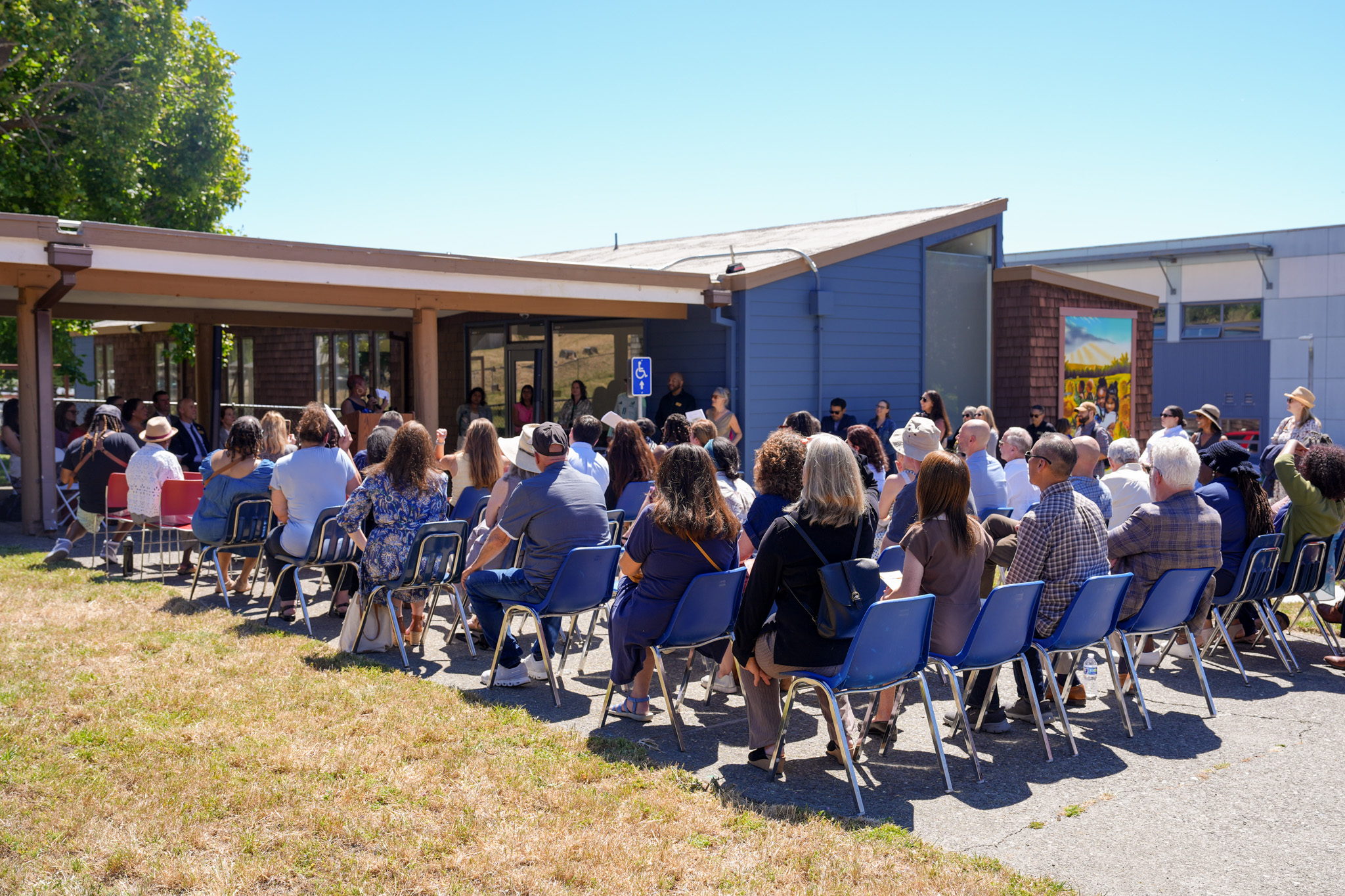 Dozens of people sit and listen to guest speakers at the ribbon-cutting event.