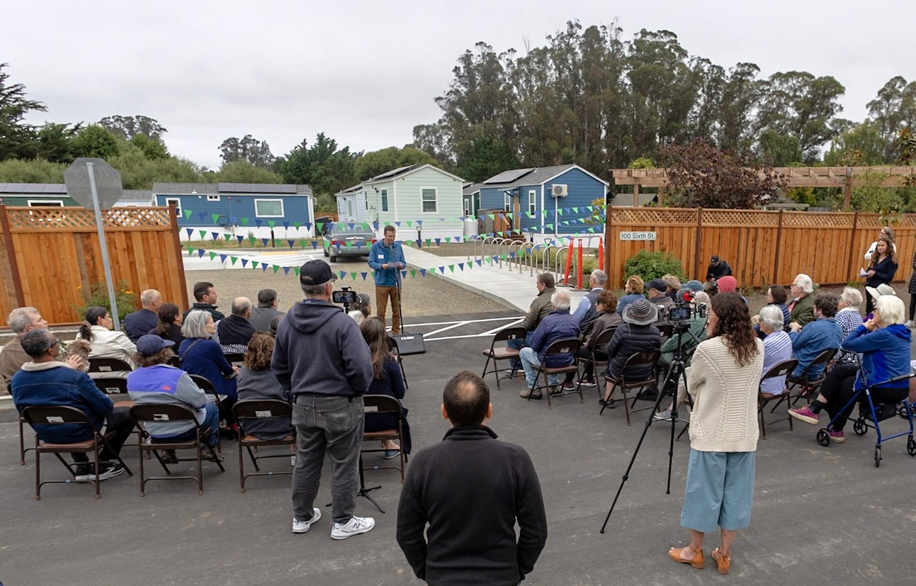 A crowd watches a speaker talk about the new homes at the Calf Lot, in the background.