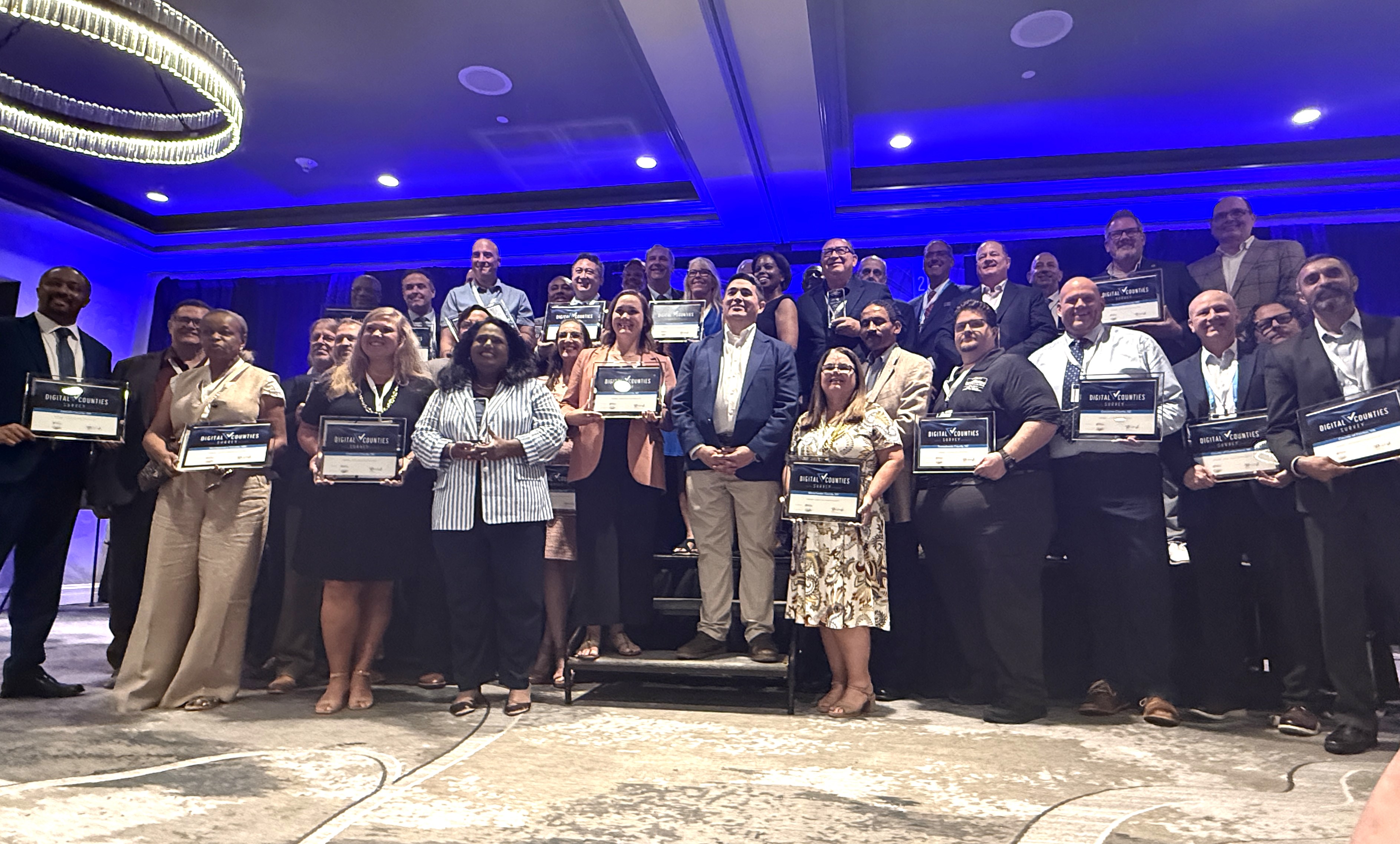 About 30 people smile and pose with plaques at the conference.