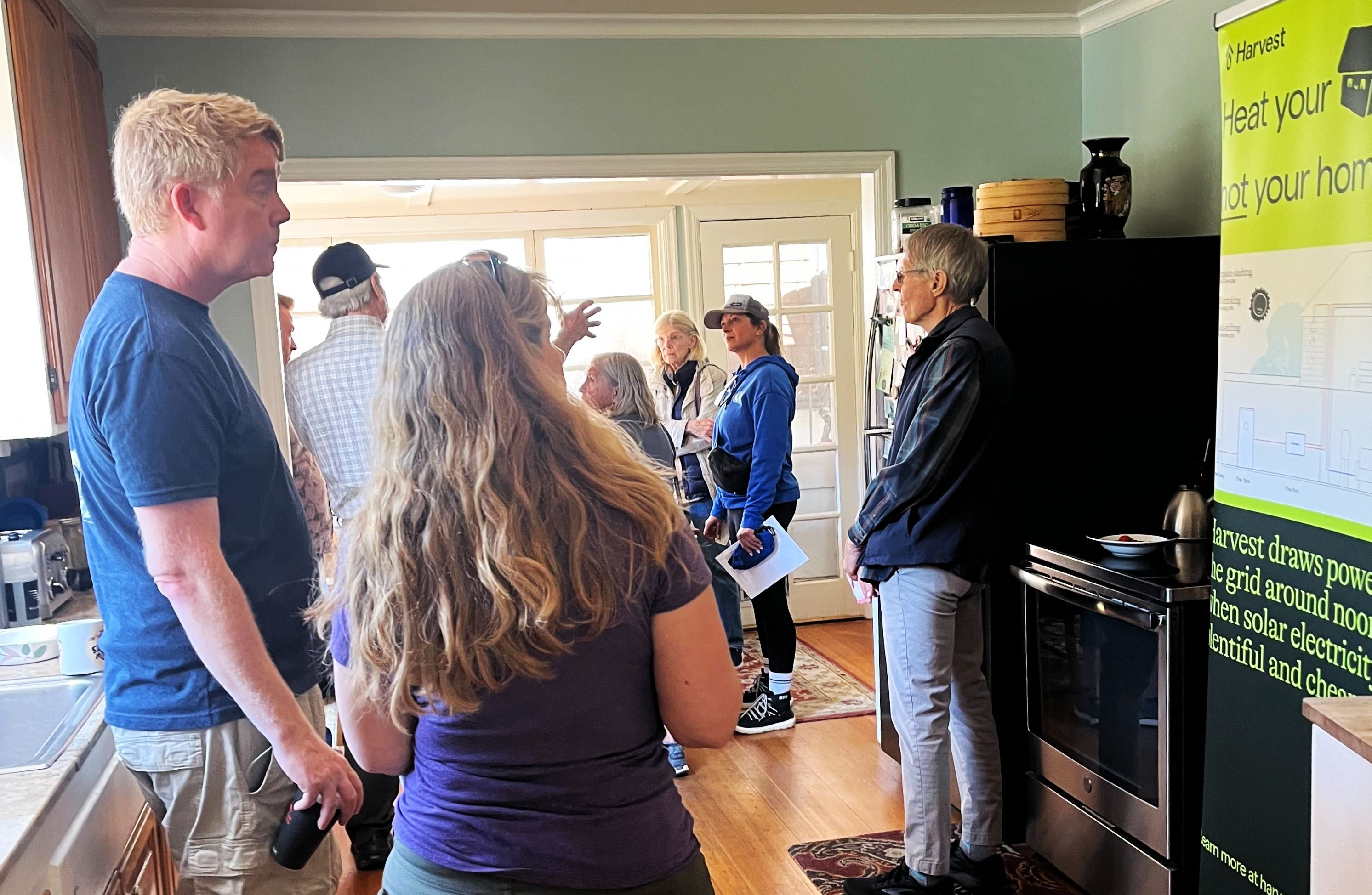 About six people stand in a kitchen and talk about the electrification of appliances during a home tour.