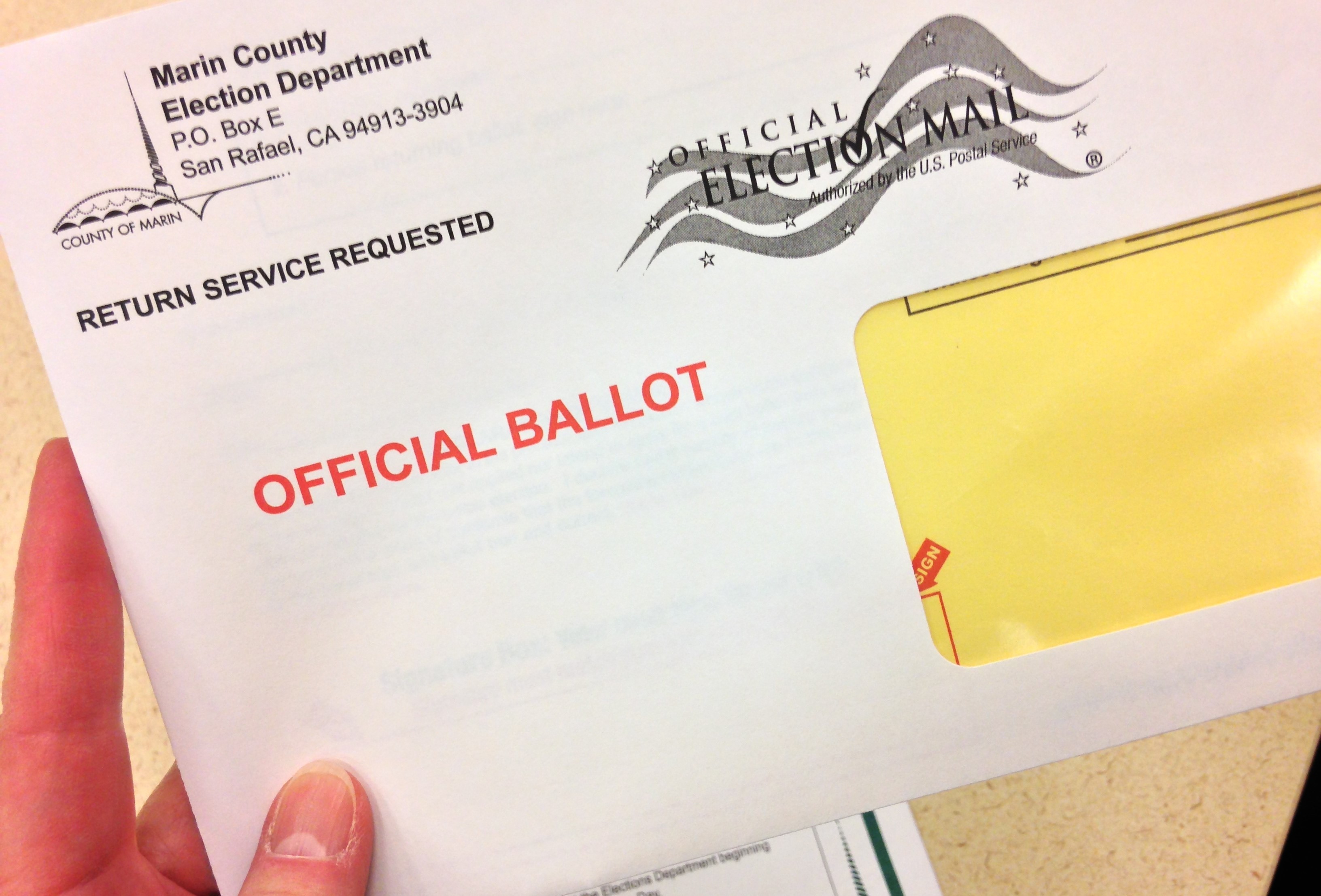 Closeup of a person's fingers holding a ballot envelope before it is mailed.