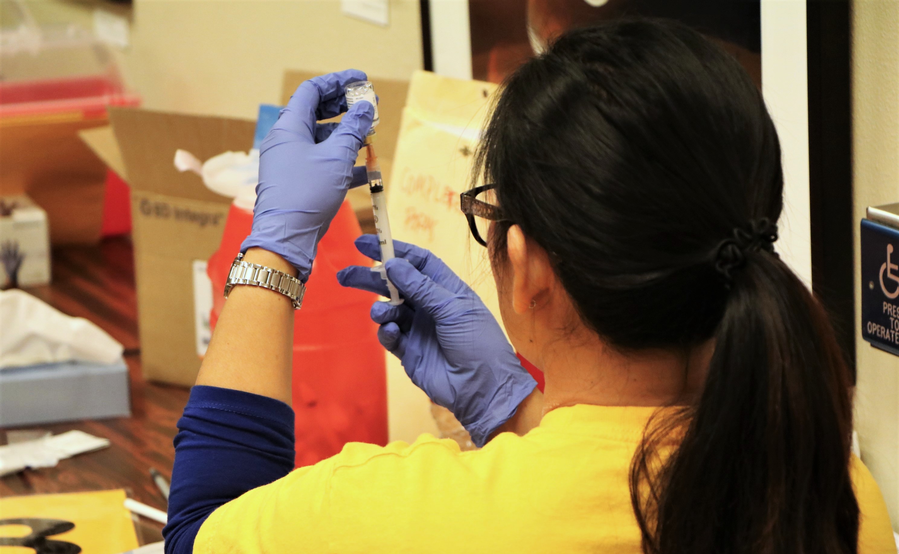 Healthcare worker wearing blue gloves prepares a vaccine syringe from a small vial.