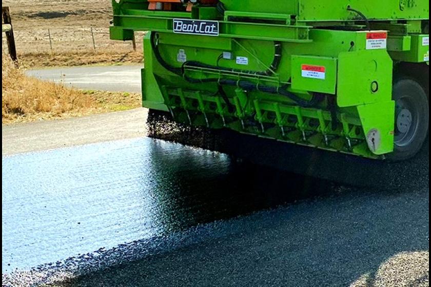 A closeup look at heavy machinery laying down tar on a road to fix the pavement. 