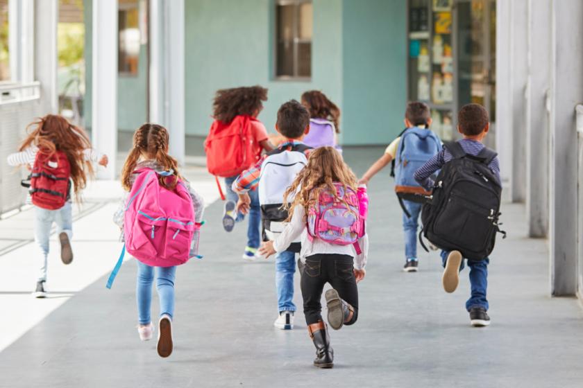 A group of young kids run down an outdoor hallway at a school.