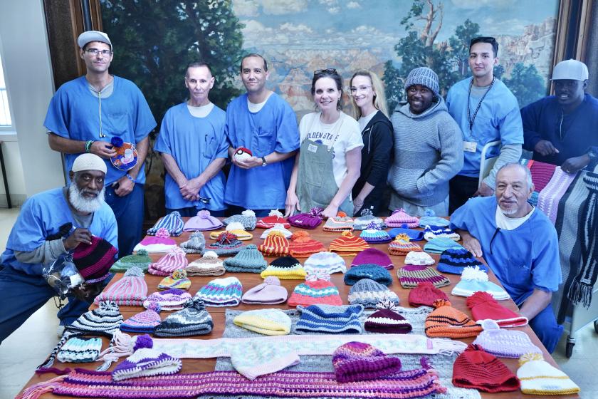 About 20 people pose around a table that displays their works of art.