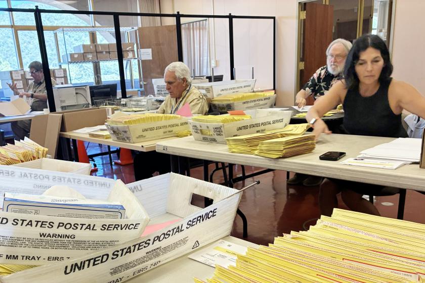 several election workers sort through ballots on a table.