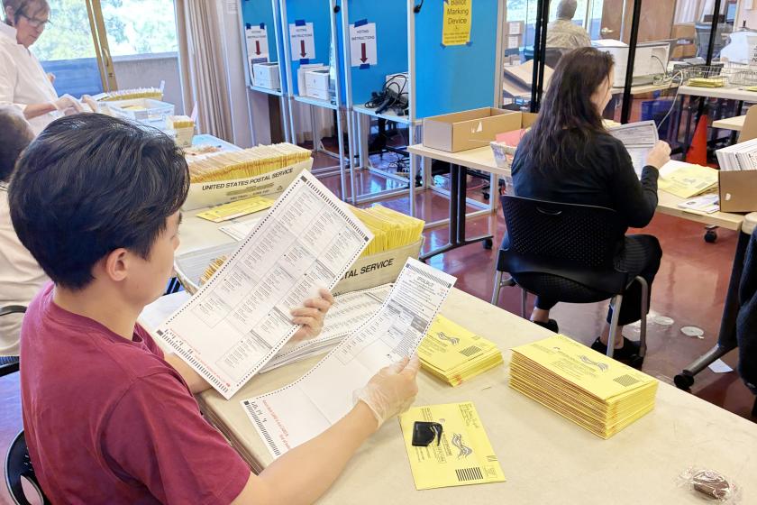 Several elections workers inspect envelopes that contain election ballots.