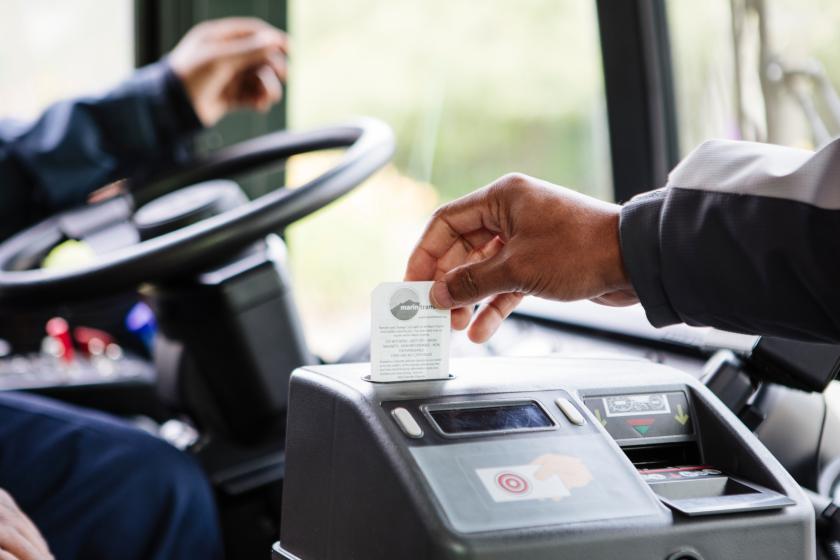 A person's hand is shown swiping a card in a scanner on a transit bus.