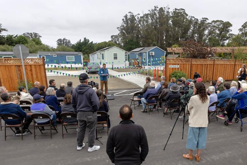 A crowd watches a speaker talk about the new homes at the Calf Lot, in the background.