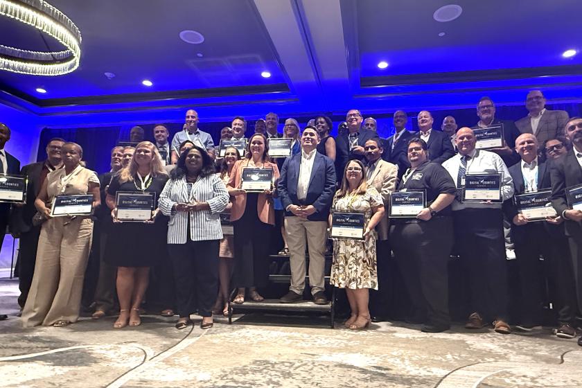 About 30 people smile and pose with plaques at the conference.