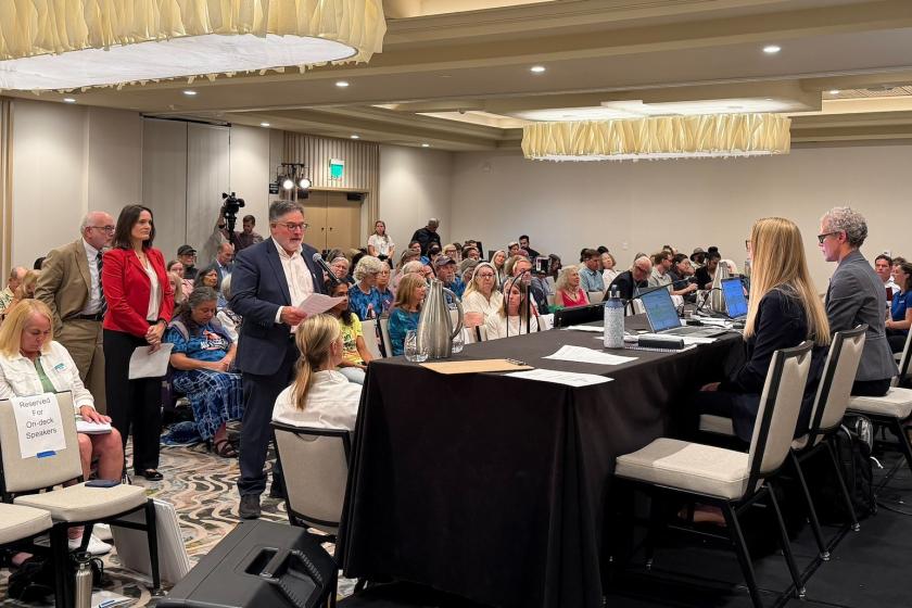 Supervisor Tennis Rodoni speaks at a lecturn during a meeting with dozens of people in attendance in the background.