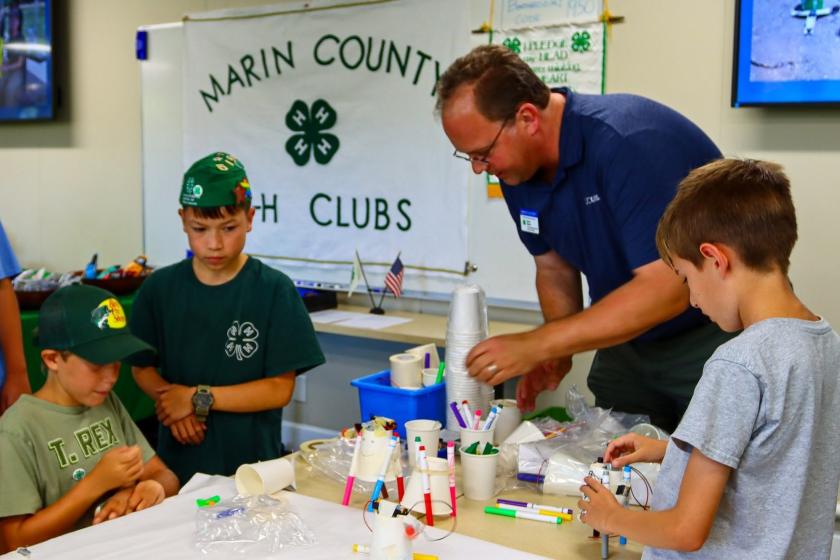 A man and three boys work at a table during a 4-H open house.