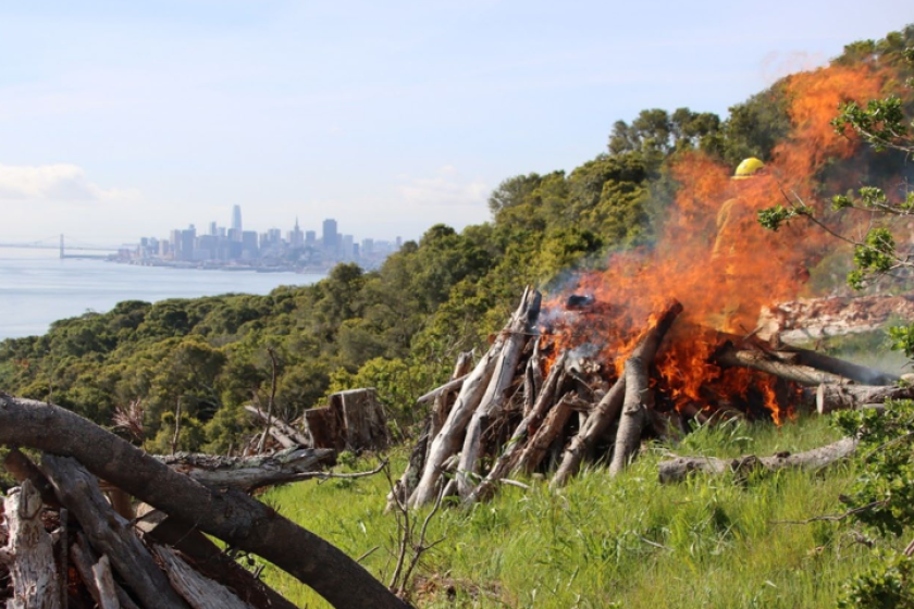 A pile of debris burns on Angel Island in 2023, with San Francisco off in the distance.