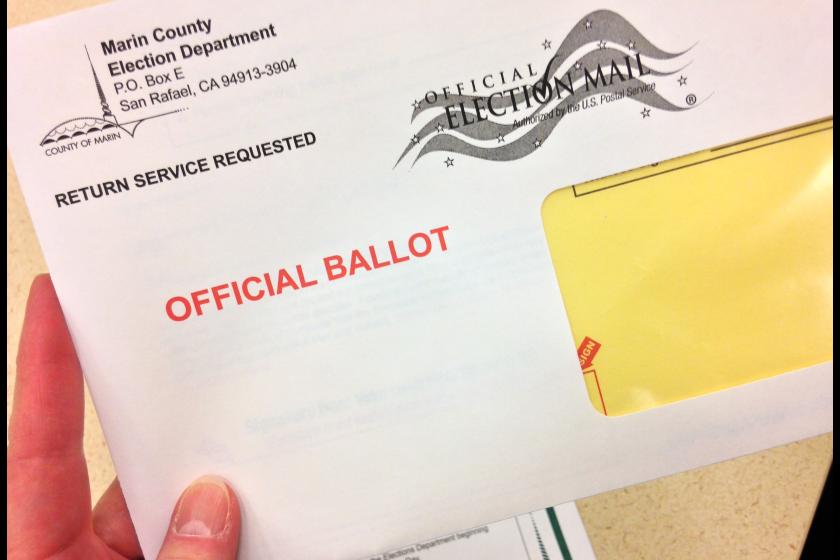Closeup of a person's fingers holding a ballot envelope before it is mailed.