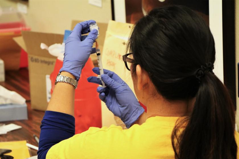 Healthcare worker wearing blue gloves prepares a vaccine syringe from a small vial.