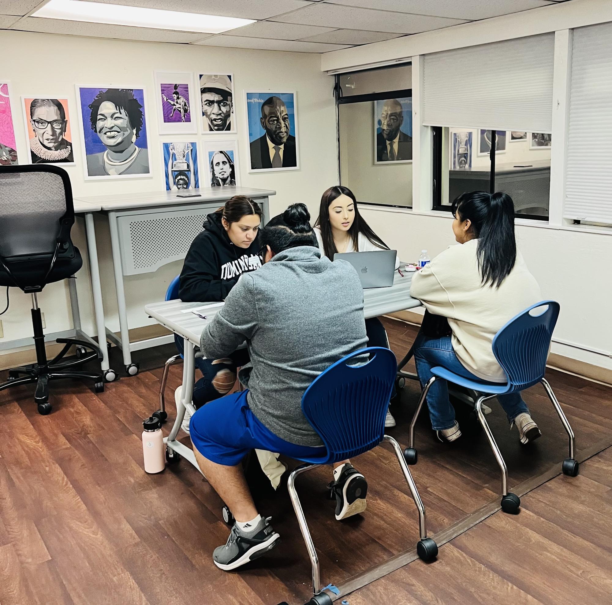 4 students work together in a classroom corner at a table with a laptop.