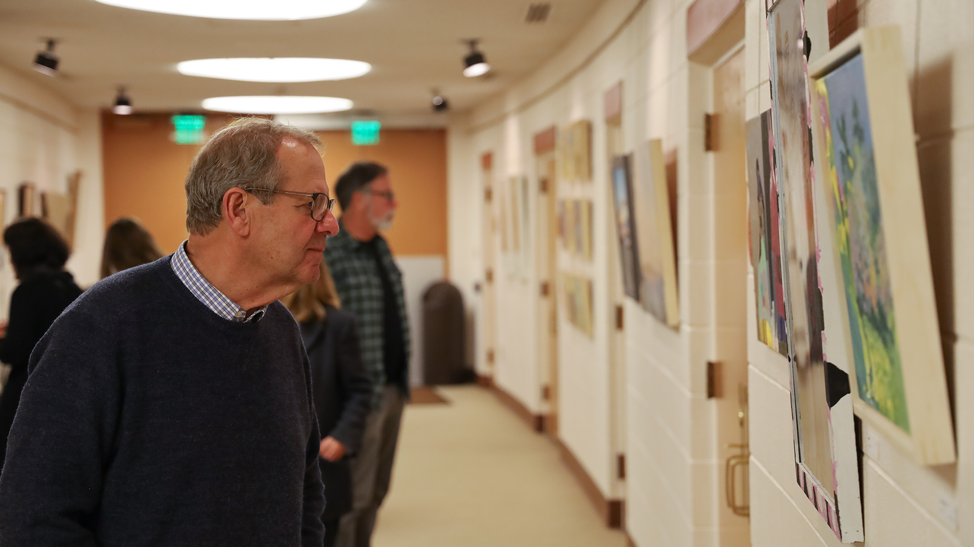 Visitors examining art work on hallway walls.