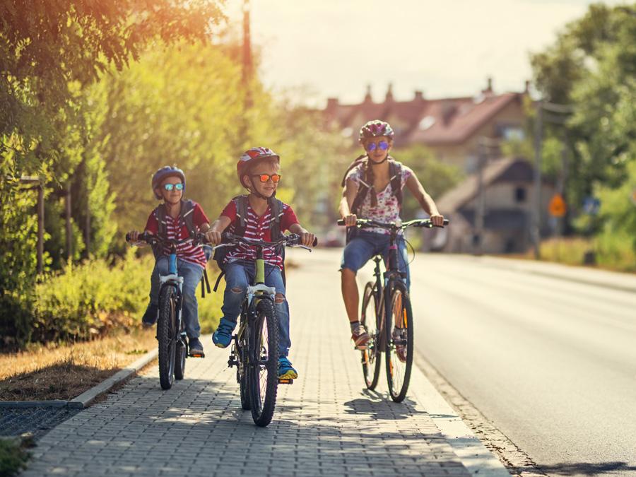Two kids and a woman ride their bikes on a sidewalk.