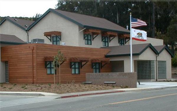 The exterior of Marin City Fire Station. It is a wood and stone building with two flags outside. 