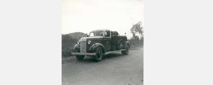 An old fire truck in the road, mountain in the background. Black and white photo.