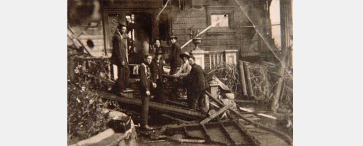  7 men standing on the porch of a wooden building. Black and white photo. 