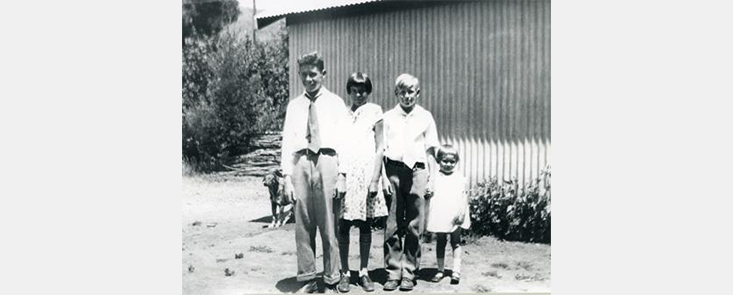4 children standing in front of a building in formal clothes. Black and white photo.