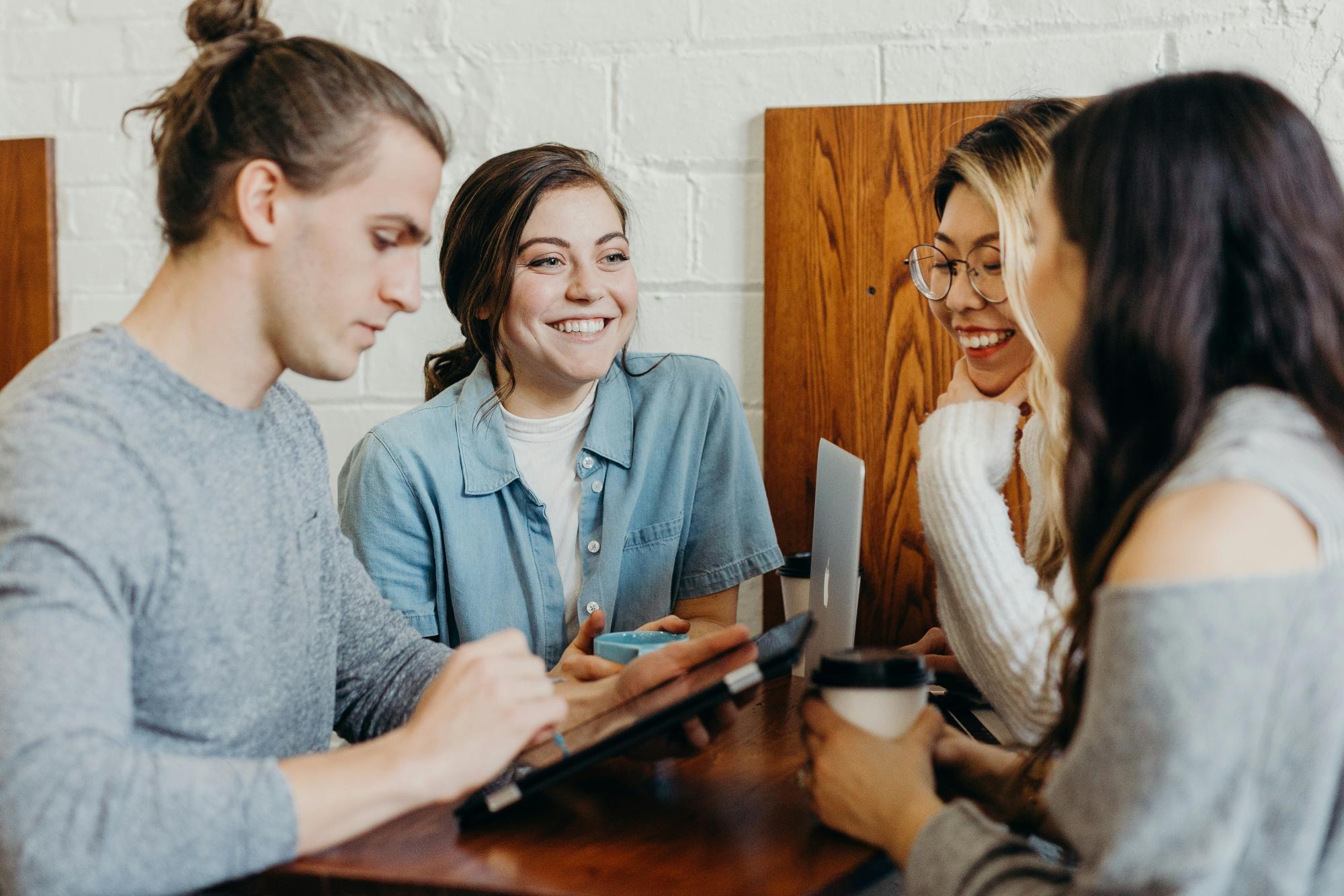 Group of four young adults sitting around a table, smiling and chatting.