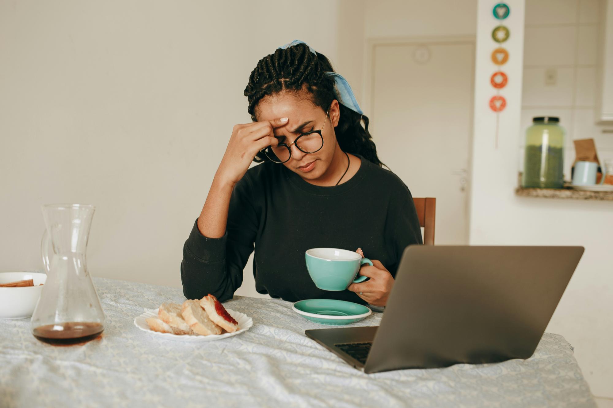 A person sitting at a table, enjoying tea and food while thinking, with a computer in front of them.