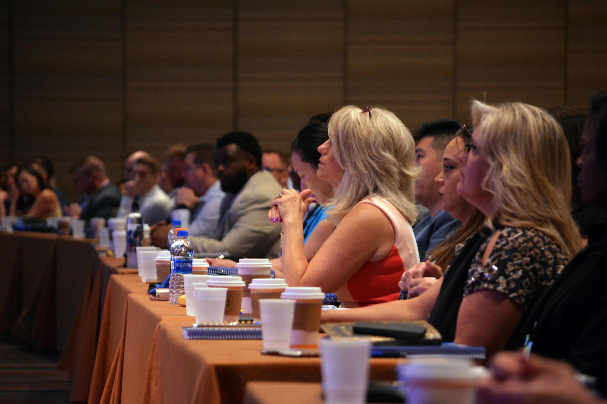 A large group gathered around a table, watching a presenter at a training event.