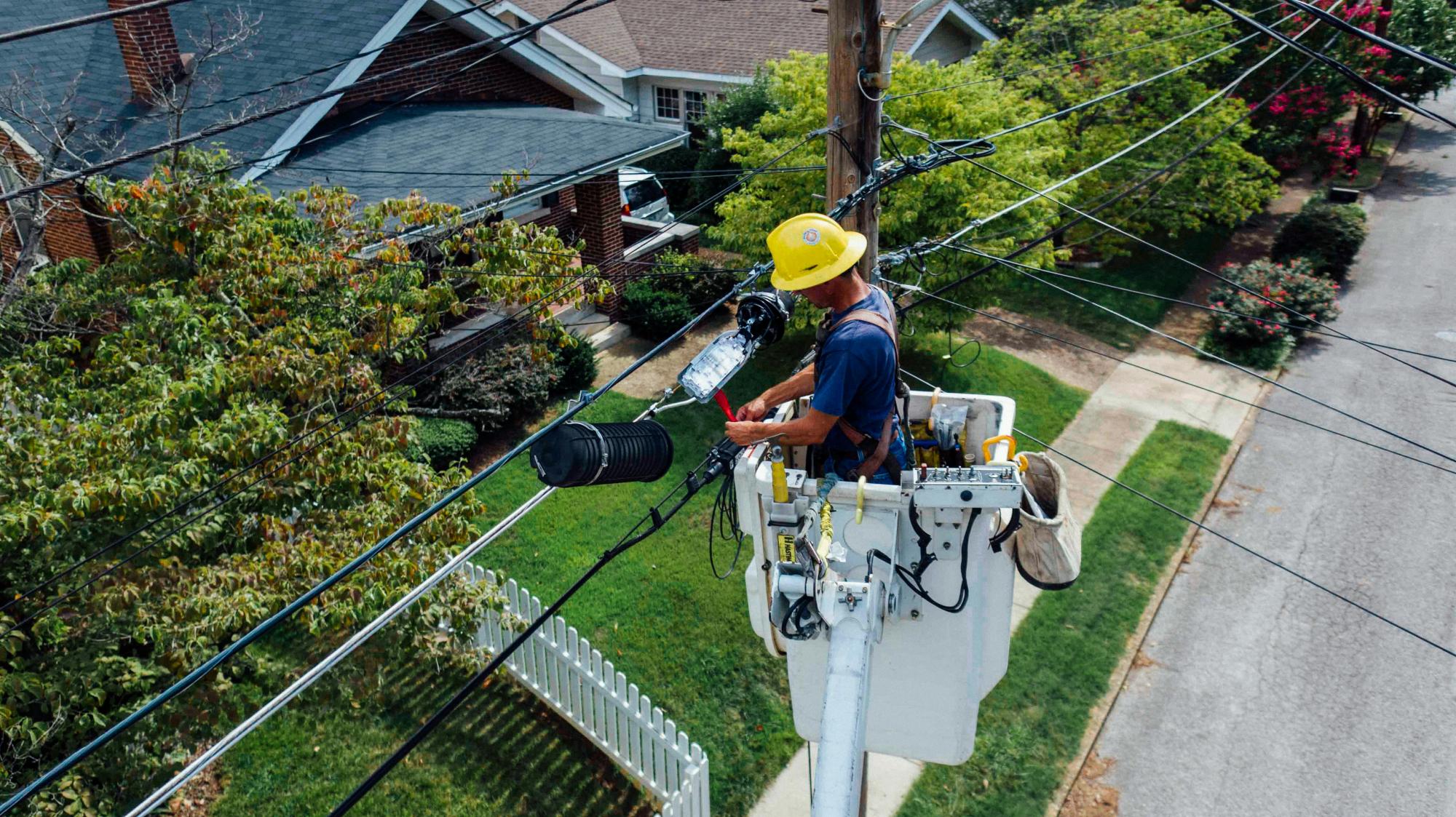 Worker inspecting electrical lines at the top of an electric pole.