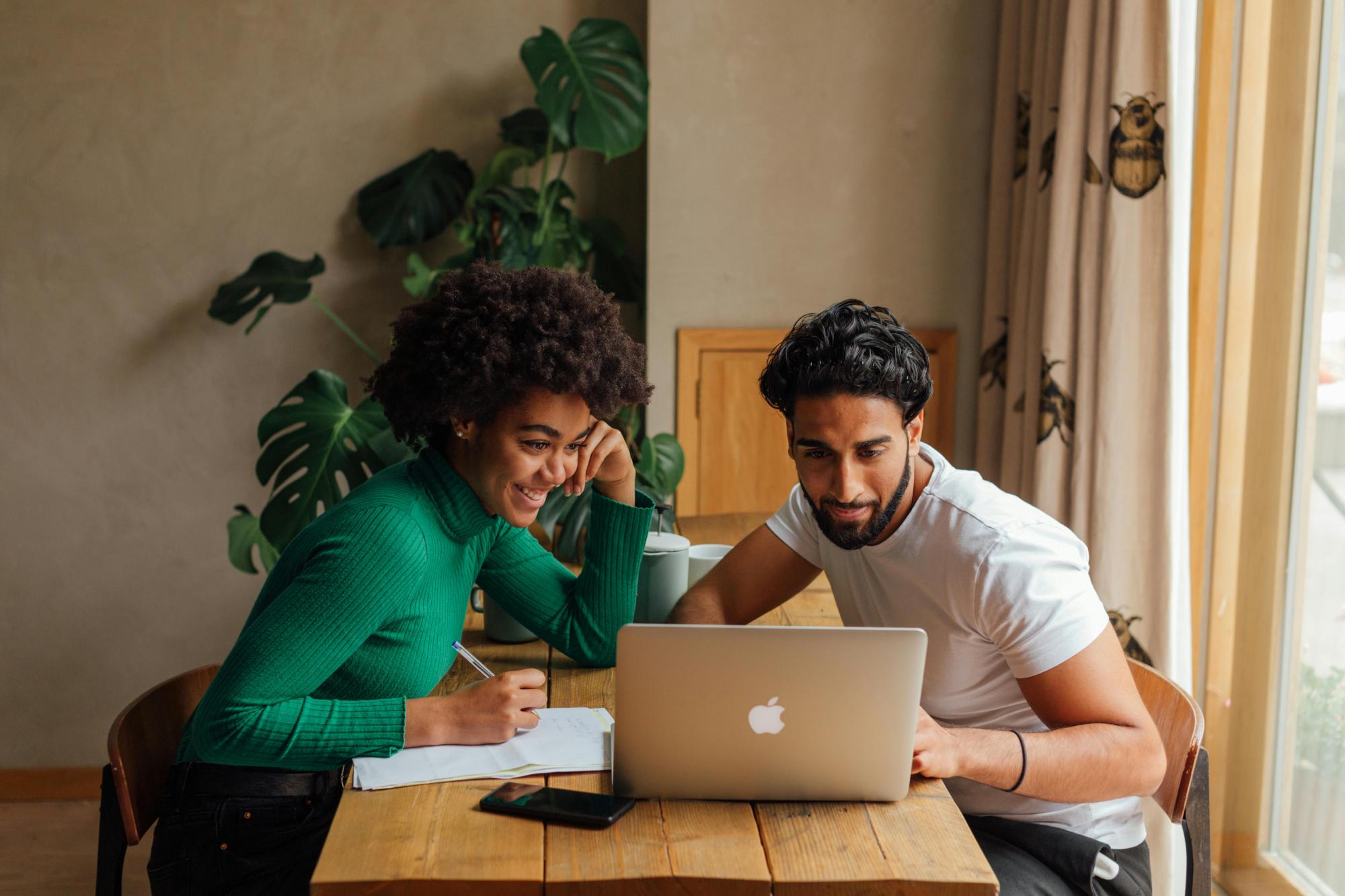 Two people collaborating at a table, sharing ideas while using a laptop and taking notes.