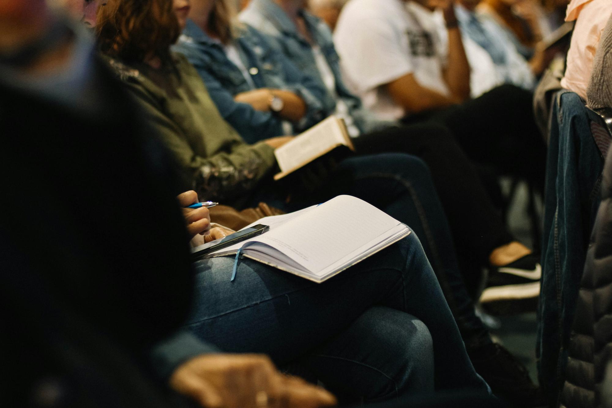 People sitting and attending a conference, taking notes.