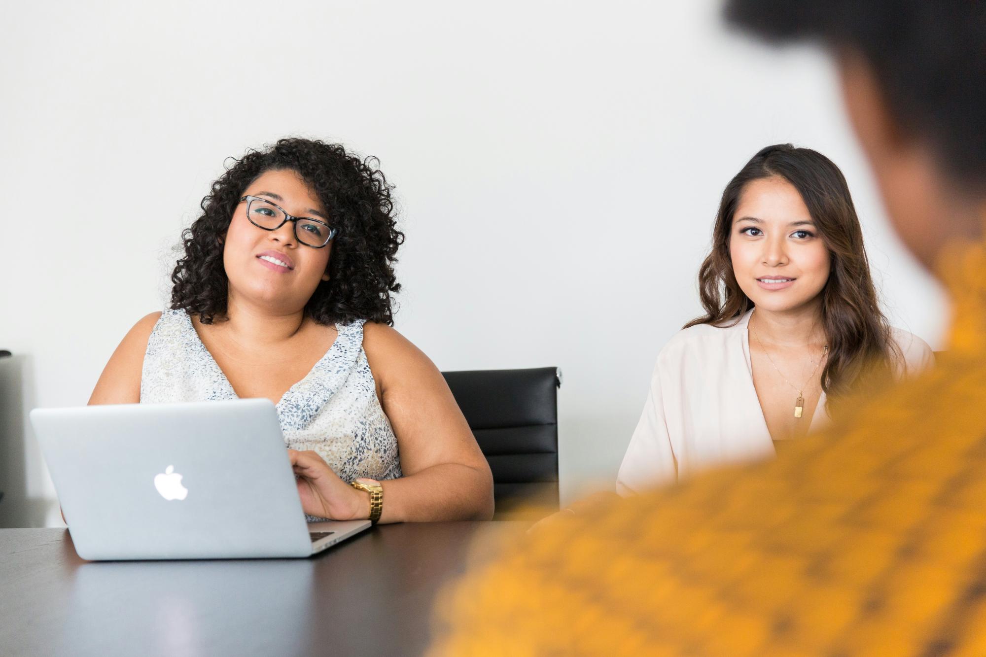 Three people holding a meeting around a table, one of them is in front of a computer