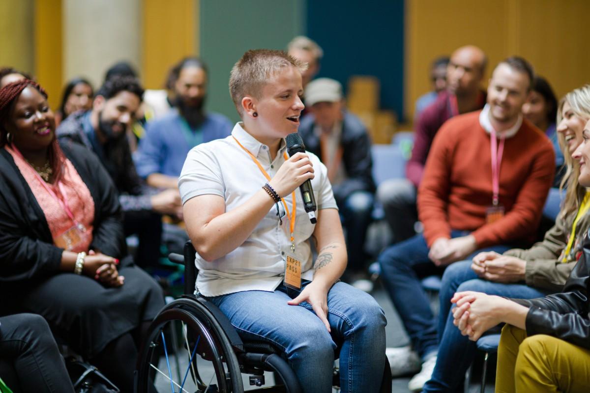 Person speaks into a microphone during a group discussion in a conference setting.