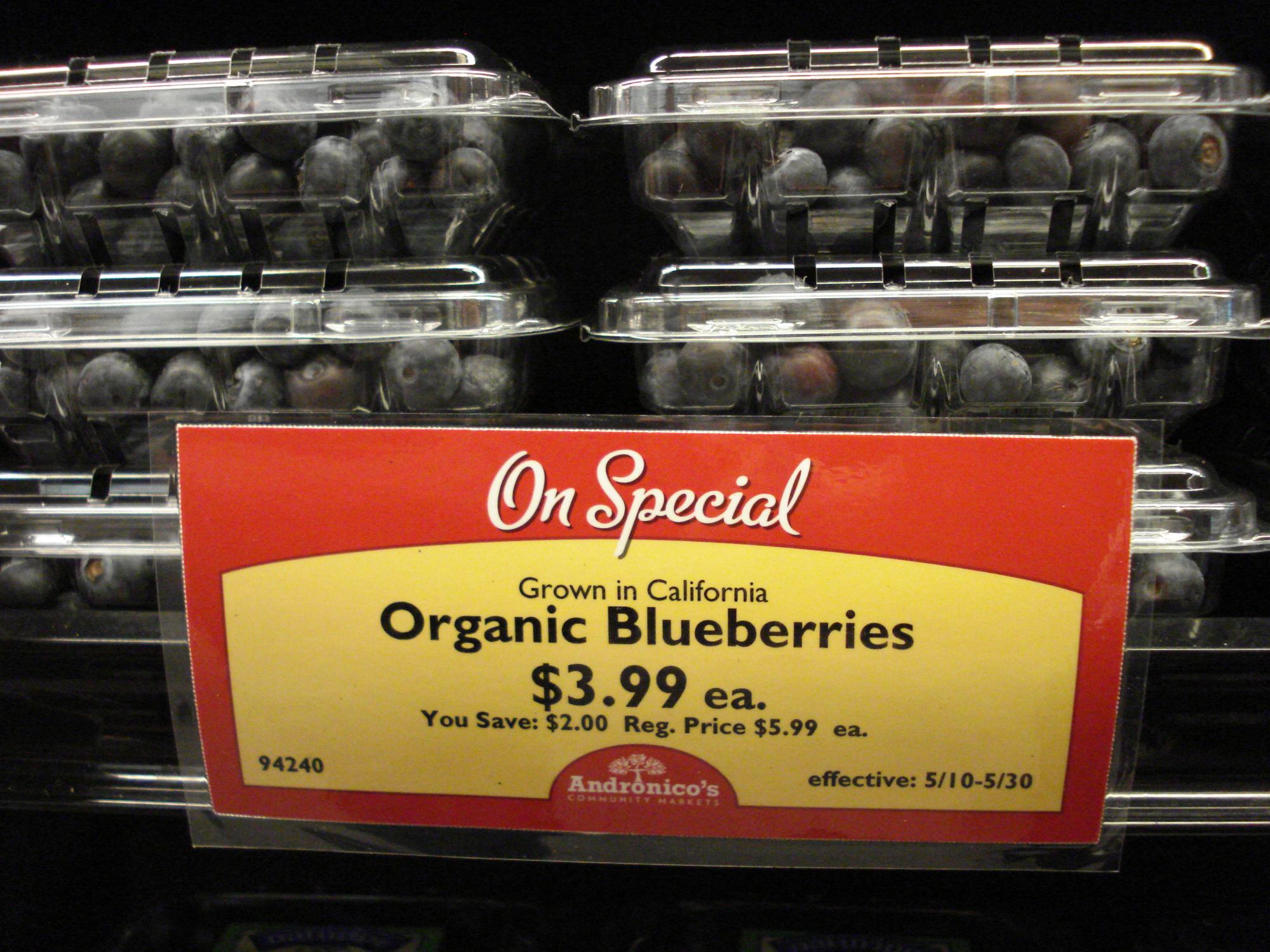 Blueberry containers displayed behind a grocery store sale sign advertising organic blueberries for $3.99.